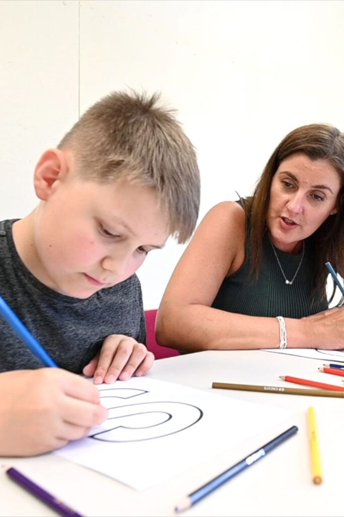 Woman next to a boy colouring in