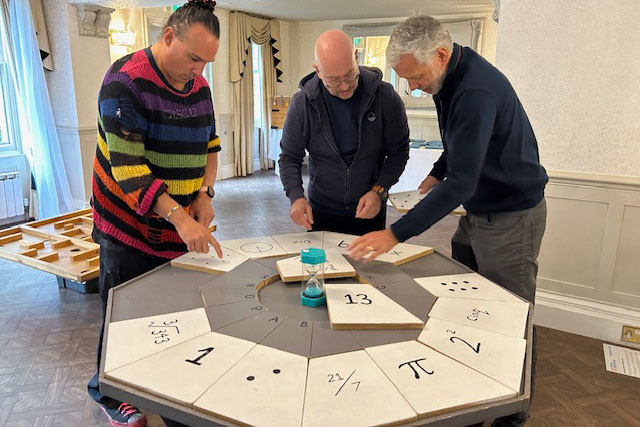 3 men solving a puzzle on a desk together