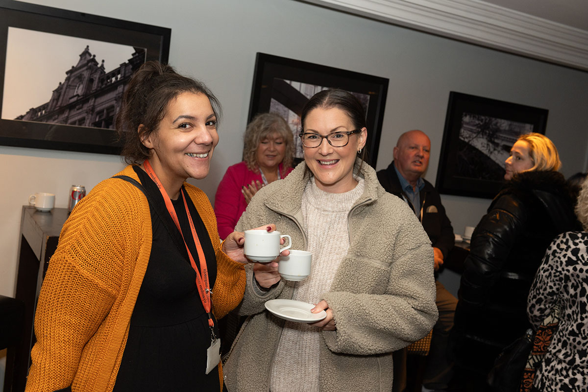 Two woman holding teas and smiling