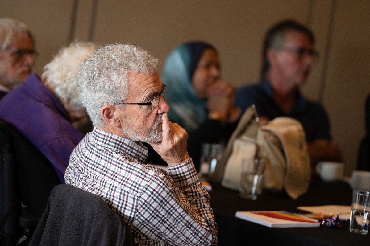 Older man at a conference with hand on mouth